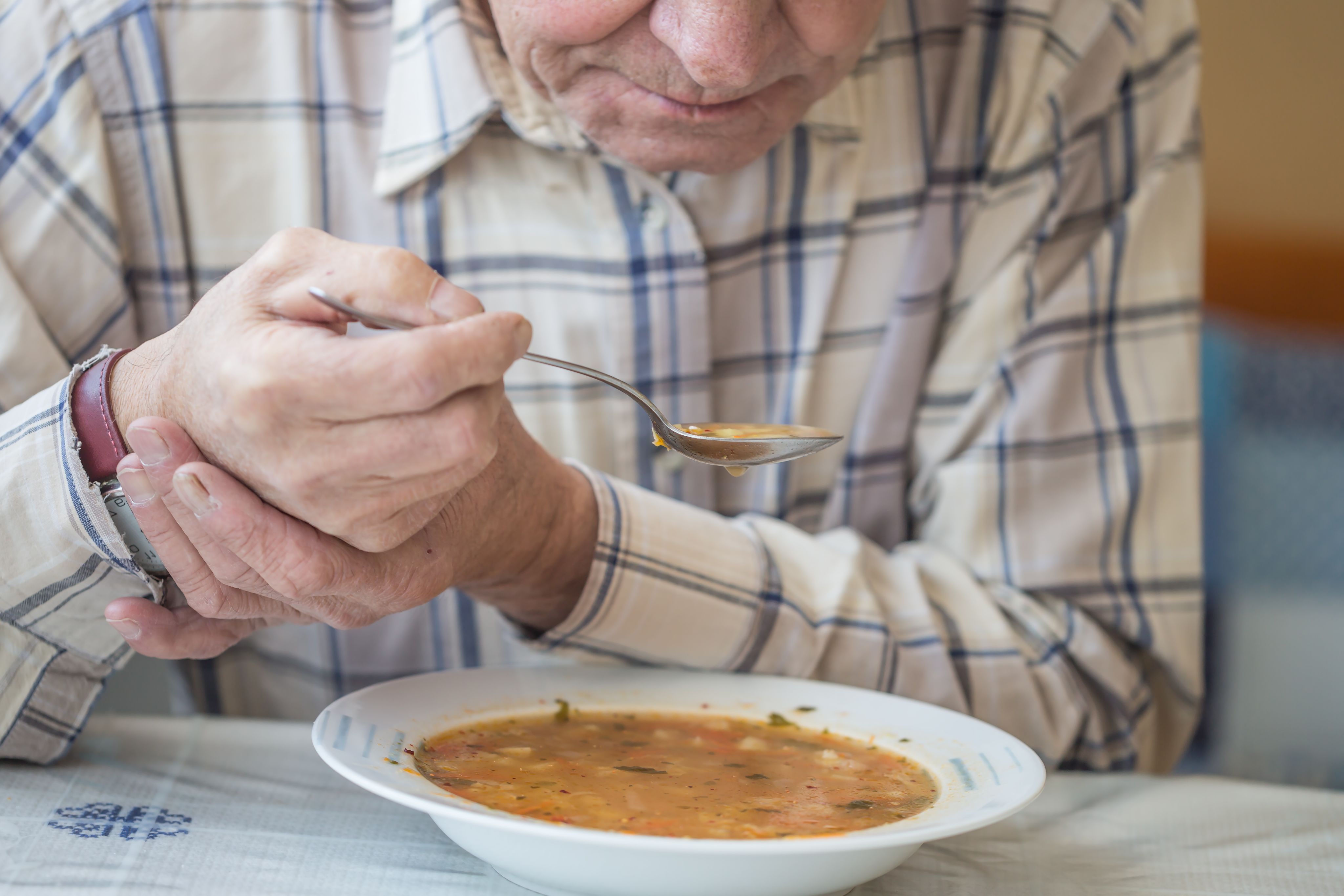 man tries to steady his trembling hand as he feeds himself